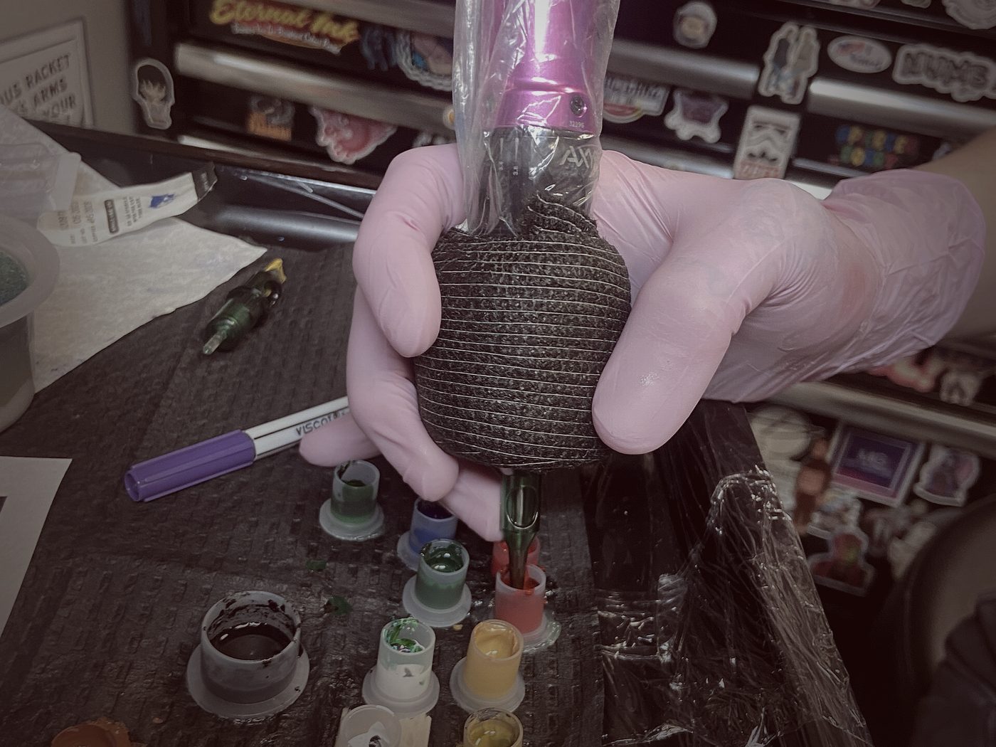 Mano enguantada sujetando un bote de tinta con c&aacute;psulas de colores